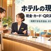ホテルのフロントで、宿泊者が財布とスマートフォンを手元に、スタッフへ穏やかに相談する場面。